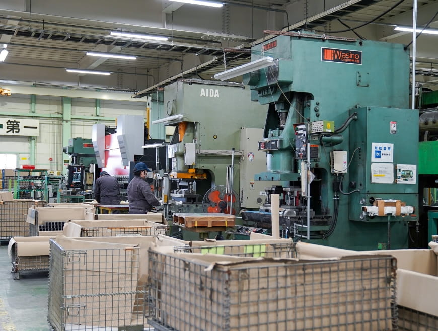 工場内に大型のプレス機械が並び、作業員が金属加工を行っている