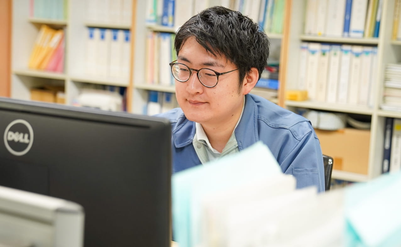 デスクでパソコンで、進捗状況の確認など作業している。