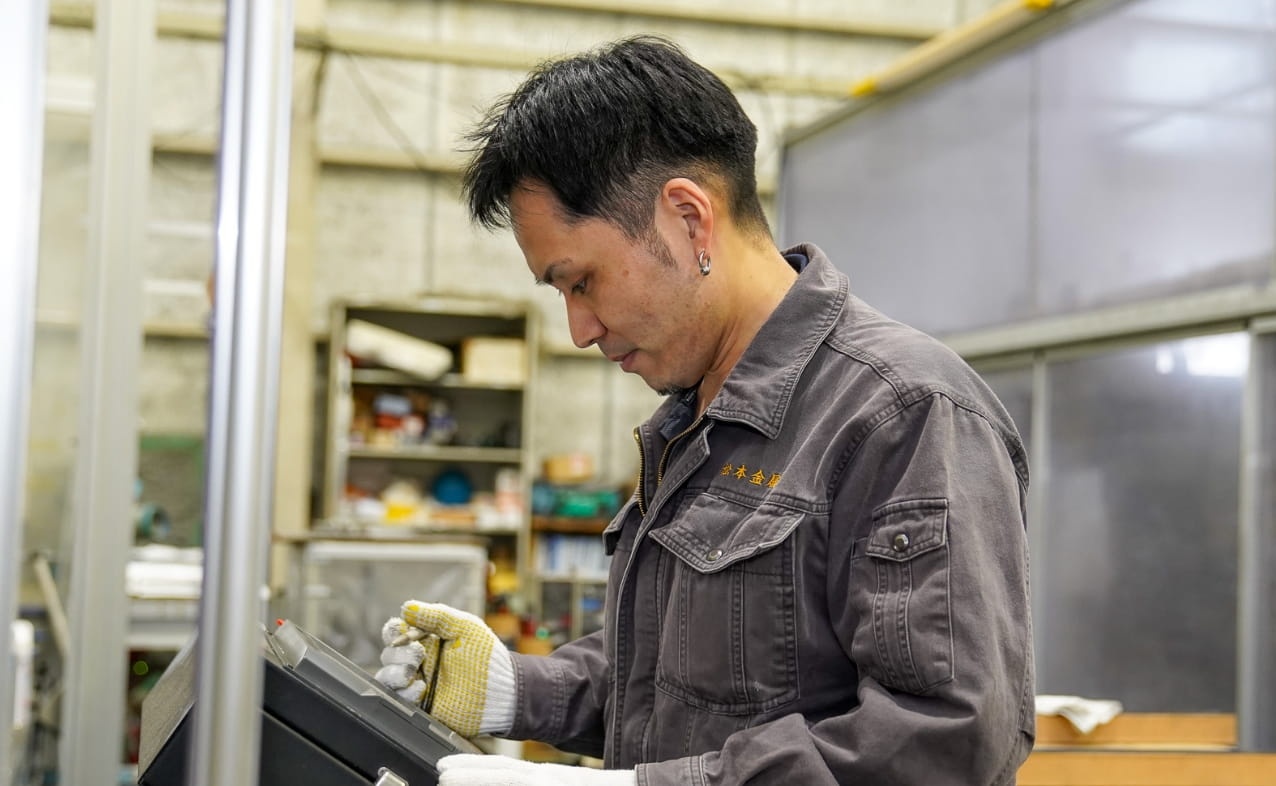 作業服を着た男性が工場内で機械や部品を確認しながら作業している。