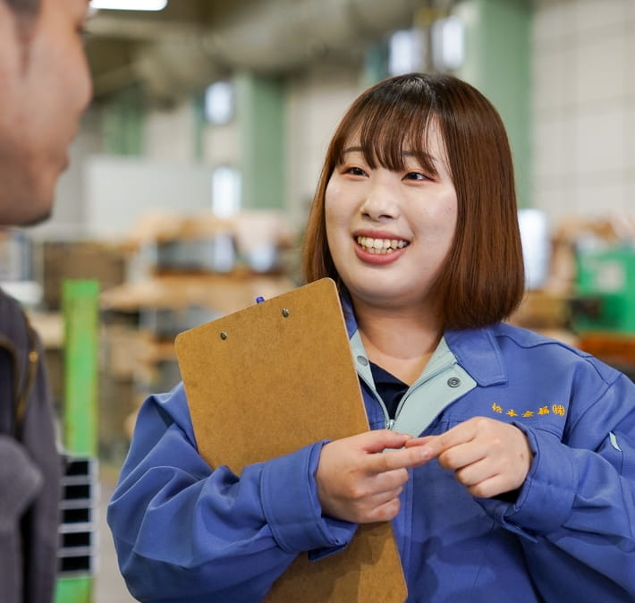 作業服を着た女性がクリップボードを持ち、笑顔で話をしている。
